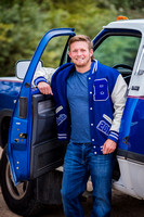 high school senior poses outside his blue truck in his letter jacket