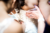 bride putting on her wedding dress with mom and sisters tying corset