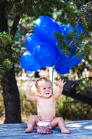 Little boy doing his 1 year smash cake session with blue balloons in the background